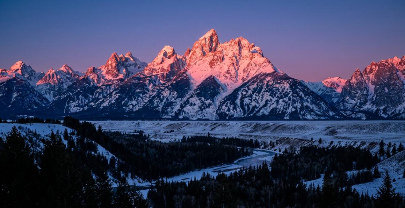 Sommets alpins baignés dans la lumière rose-orangée de l'Alpenglow avec vallée dans l'ombre