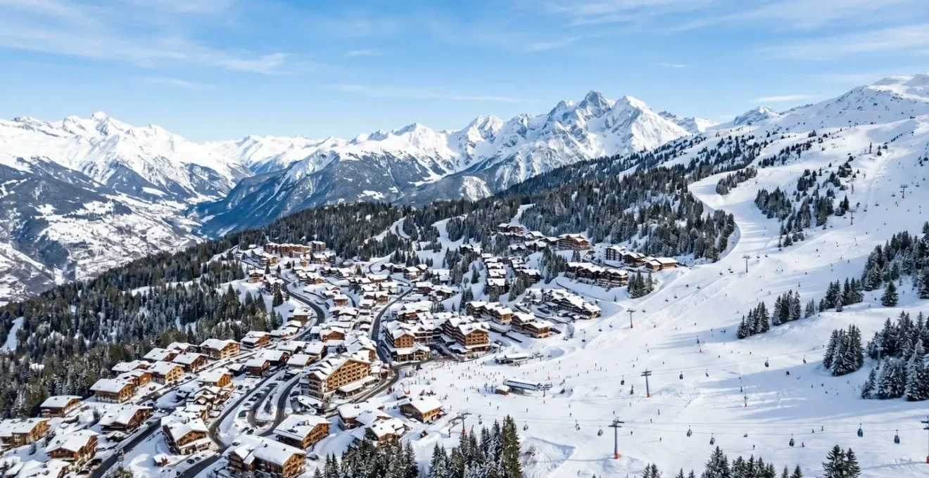 Vue panoramique sur les pistes enneigées de Courchevel 1850 avec chalets en arrière-plan par un ciel bleu alpin