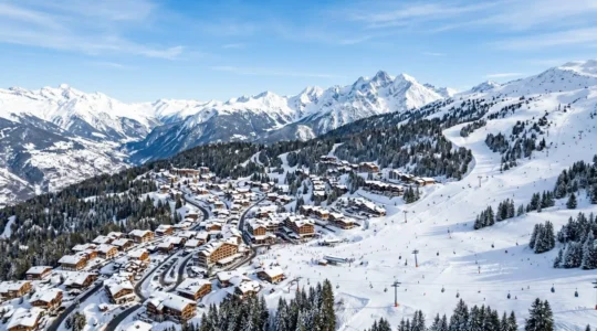 Vue panoramique sur les pistes enneigées de Courchevel 1850 avec chalets en arrière-plan par un ciel bleu alpin